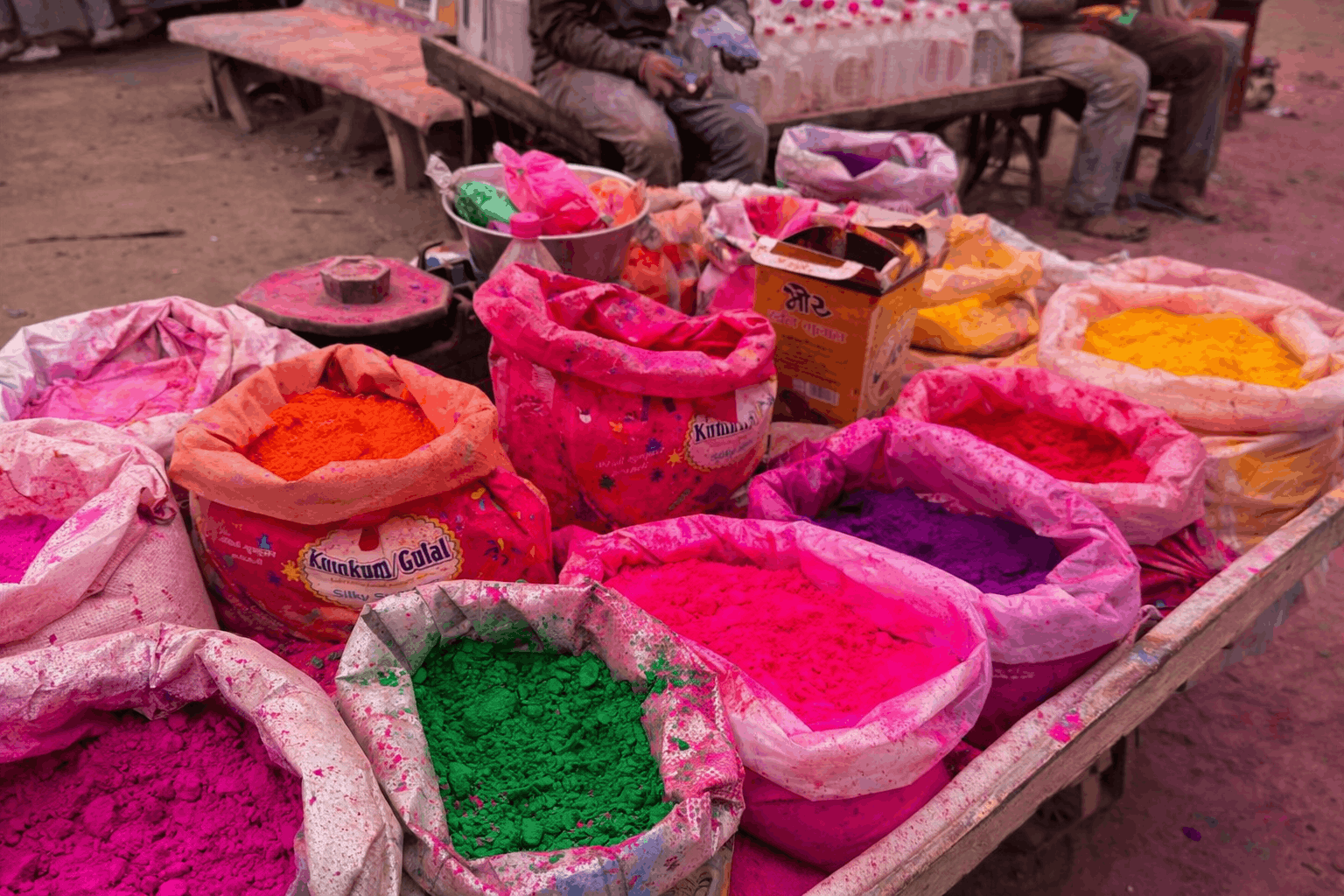 Colorful gulal powders for Holi displayed in open sacks at a local market in Rajasthan, showcasing bright pink, green, yellow, and orange colors